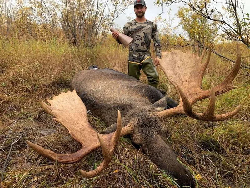 Alaska hunter Alex Bilyeu holding his Bull Magnet moose call beside a bull moose