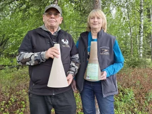 Wayne and Marilyn Kubat holding two Bull Magnet moose calls outside their shop in Wasilla, Alaska